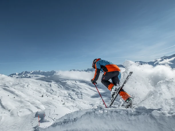 Skisprung auf der sonnigen Piste der Aletsch Arena Beim Wahltages Skipass Aletsch Arena springt ein Skifahrer mit Schwung über eine Schneekante und geniesst den Moment in der klaren Winterluft