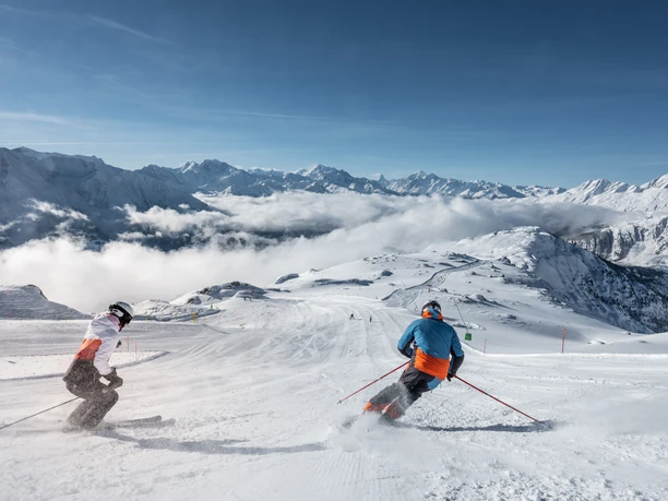 Dynamisches Skifahren mit Blick auf die Walliser Alpen Beim Wahltages Skipass Aletsch Arena fahren zwei Skifahrer in eleganten Schwüngen über die breite Panoramapiste mit Blick auf die Walliser Alpen