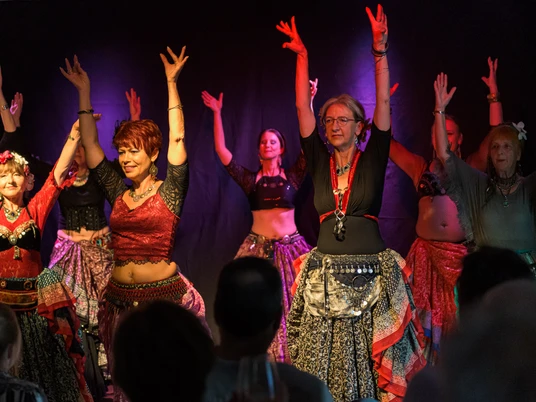 Kulturnacht Wolfenbüttel 2023,DSC_4130.jpg Tanzgruppe in bunten Kleidern hebt die Arme bei bunter Beleuchtung.