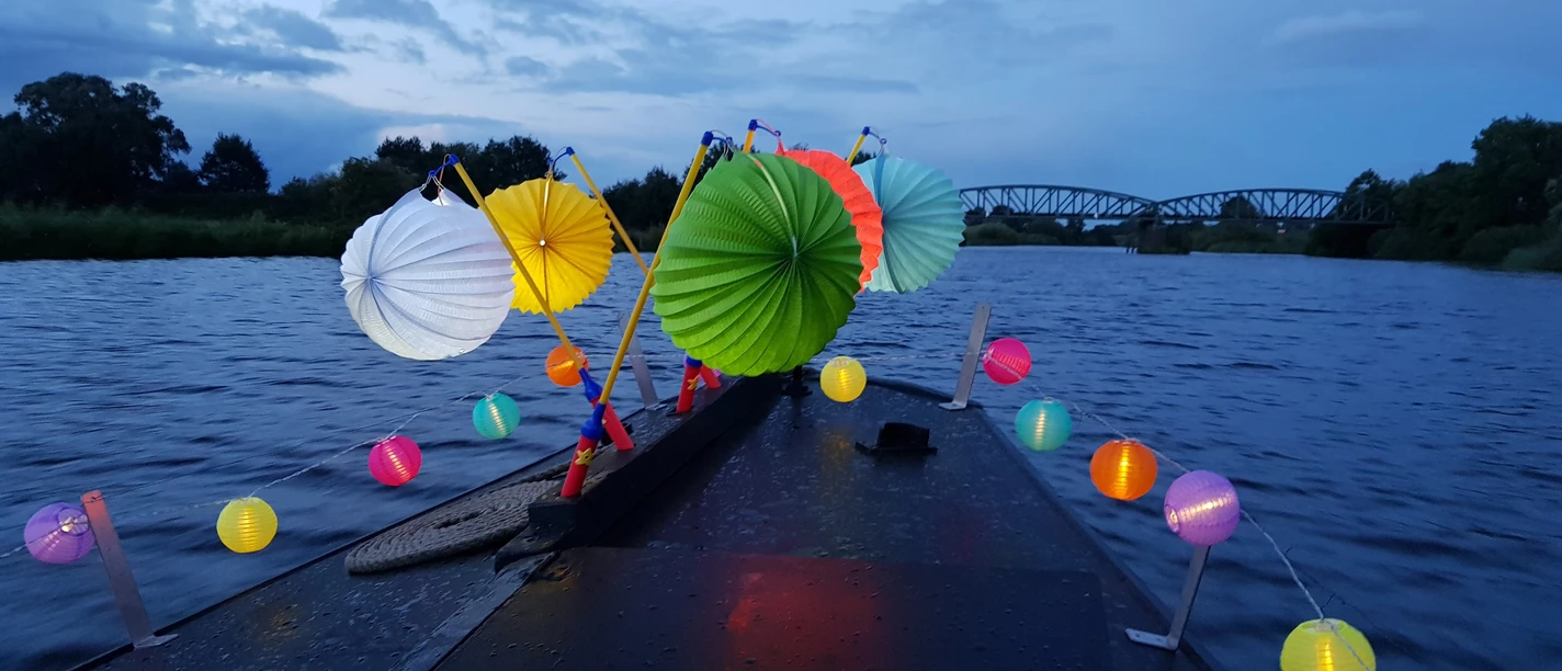 Lampionfahrt auf der Hamme Colorfully illuminated lanterns on a boat at dusk on the Hamme with a bridge in the background.