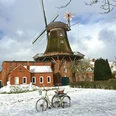 Mühle Pewsum im Winter Zu sehen ist die Mühle Pewsum im Winter, es liegt ein bisschen Schnee, im Vordergrund steht ein altes Fahrrad als Deko.You can see the Pewsum mill in winter, there is a bit of snow, in the foreground is an old bicycle as decoration.Man kan se Pewsum-møllen om vinteren, der er lidt sne, og i forgrunden står en gammel cykel som dekoration.Je ziet de Pewsum molen in de winter, er ligt een beetje sneeuw, op de voorgrond staat een oude fiets als decoratie.