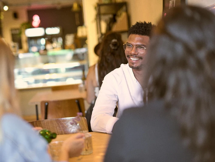 Ein helles Café mit freundlicher Atmosphäre. Gäste sitzen entspannt miteinander an Holztischen.