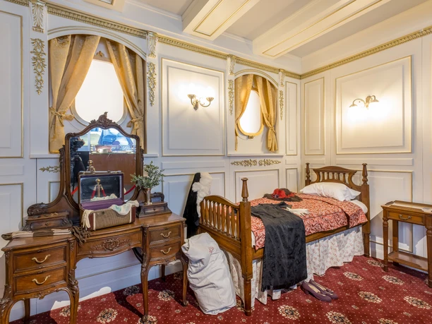 Photo of a replica passenger room on the Titanic with dressing table, bed and bedside table in the exhibition "Titanic: An Immersive Voyage"