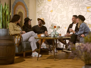 Das KAFF, Mülheim an der Ruhr Gruppe aus jungen Erwachsenen in einer modernen und gemütlichen Lounge-Ecke eines Cafés mit stilvoller Deko und Wandkunst.