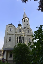 Klosterkirche Helle Klosterkirche mit hohem Turm, spitzem Dach und rundbogigen Fenstern vor blauem Himmel.