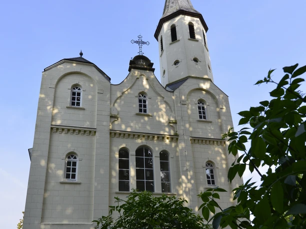 Klosterkirche Helle Klosterkirche mit hohem Turm, spitzem Dach und rundbogigen Fenstern vor blauem Himmel.