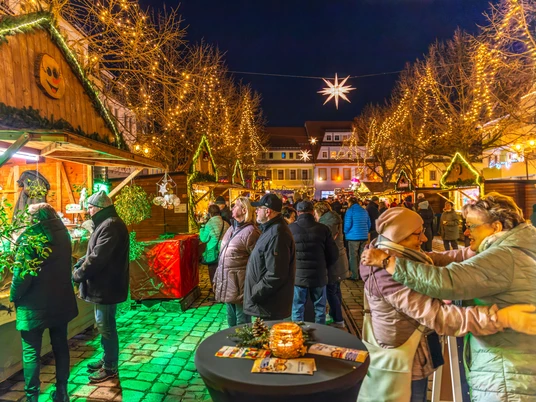 Weihnachtsmarkt Döbeln - Weihnachten in der Region Leipzig Der Weihnachtsmarkt in Döbeln zeigt eine stimmungsvolle Szenerie mit leuchtenden Lichtern und fröhlichen Menschen, die die festlich geschmückten Holzbuden erkunden. Die warme Beleuchtung und der Sternenhimmel schaffen eine einladende Atmosphäre, während Besucher in Winterkleidung zwischen den Ständen flanieren.