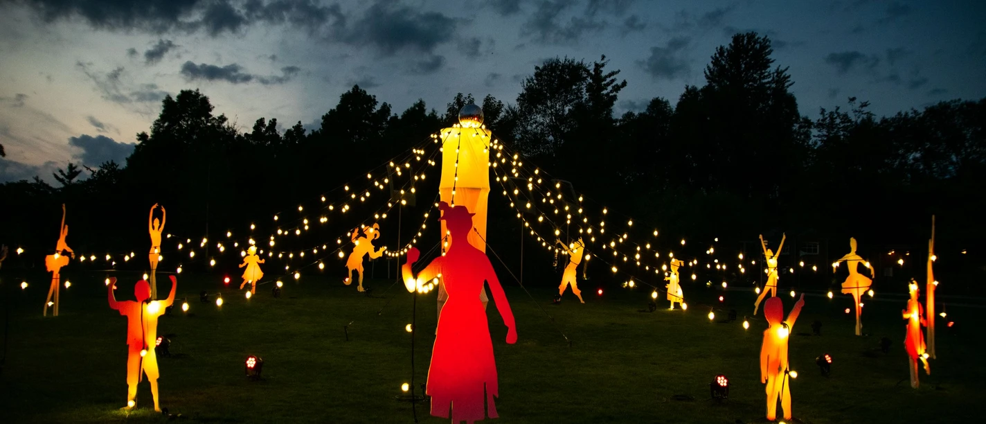 PdG_Illumination_2025_01.jpg Beleuchtete Figuren tanzen unter Lichterketten auf einer Wiese vor dunklem Abendhimmel.