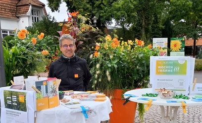 Reiner Dunker, Energieexperte Verbraucherzentrale Niedersachsen.jpg Ein Mann mit Infostand zur Energieberatung vor blühenden Pflanzen im Freien.