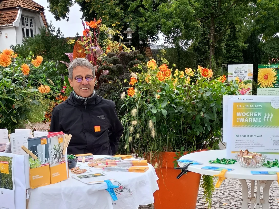 Reiner Dunker, Energieexperte Verbraucherzentrale Niedersachsen.jpg Ein Mann mit Infostand zur Energieberatung vor blühenden Pflanzen im Freien.
