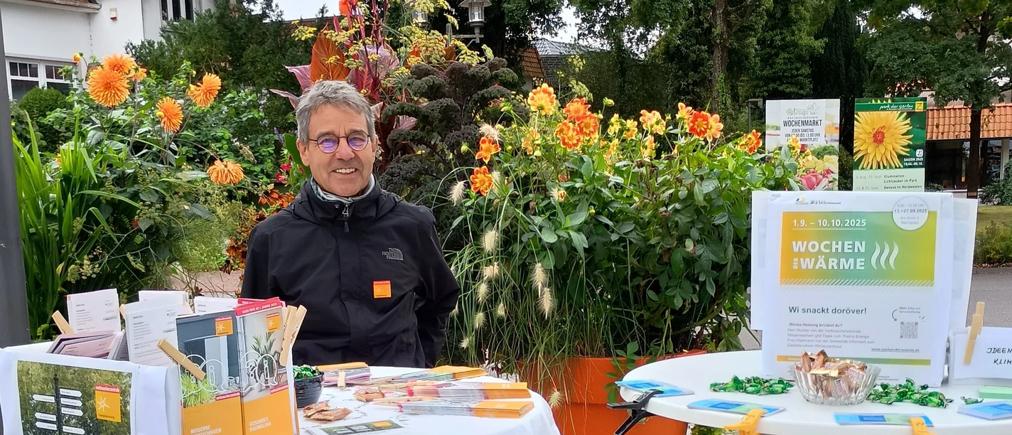 Reiner Dunker, Energieexperte Verbraucherzentrale Niedersachsen.jpg Ein Mann mit Infostand zur Energieberatung vor blühenden Pflanzen im Freien.