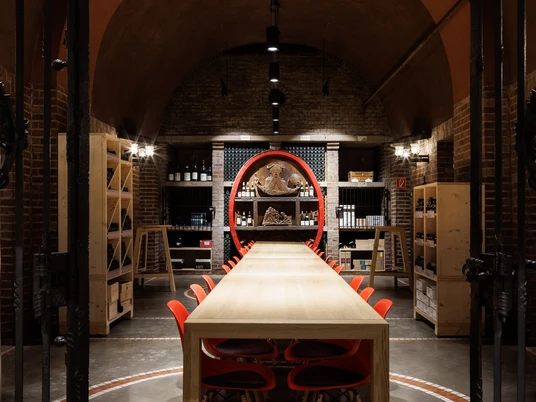 Cologne wine cellar Langer Holztisch mit roten Stühlen in einem stimmungsvoll beleuchteten Weinkeller.Long wooden table with red chairs in an atmospherically lit wine cellar.