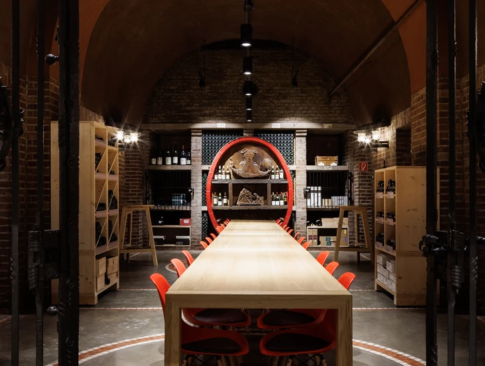 Cologne wine cellar Langer Holztisch mit roten Stühlen in einem stimmungsvoll beleuchteten Weinkeller.Long wooden table with red chairs in an atmospherically lit wine cellar.