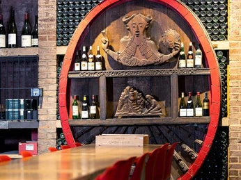 Cologne wine cellar Ein Weinkeller mit hölzerner Relieftafel und Weinflaschen in Regalen entlang einer Ziegelwand.A wine cellar with a wooden relief panel and wine bottles on shelves along a brick wall.