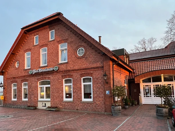 Zur Nordseite Backsteingebäude mit roten Dachziegeln, gepflastertem Hof und dem Schriftzug „Zur Nordseite“.