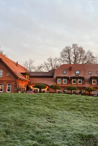 Restaurant und Hotel "Zur Nordseite" Backsteinbau mit rotem Dach in winterlicher Morgensonne, davor frostbedeckte Wiese und Bäume.