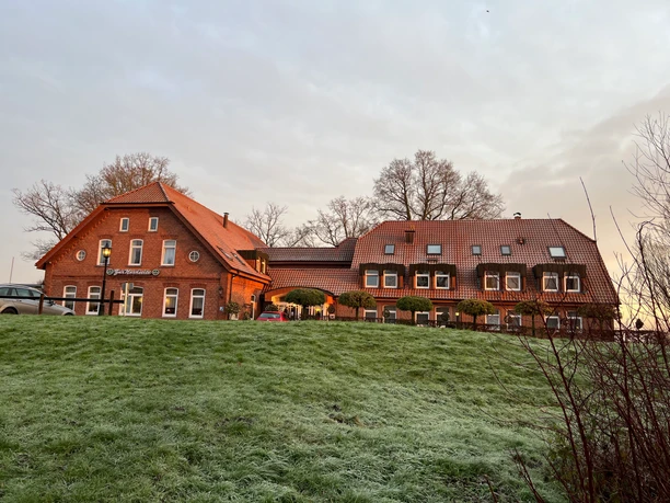Restaurant und Hotel "Zur Nordseite" Backsteinbau mit rotem Dach in winterlicher Morgensonne, davor frostbedeckte Wiese und Bäume.