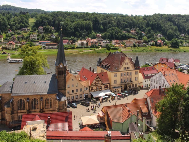View of a small riverside town with a church, colorful houses and green hills.