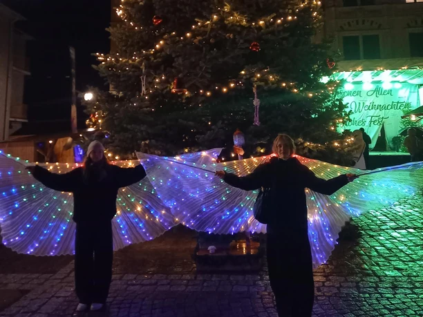 Weihnachtsmarkt Bad Lausick - Weihnachten in der Region Leipzig Ein Weihnachtsbaum in Bad Lausick, beleuchtet und flankiert von Menschen mit leuchtenden Flügeln.