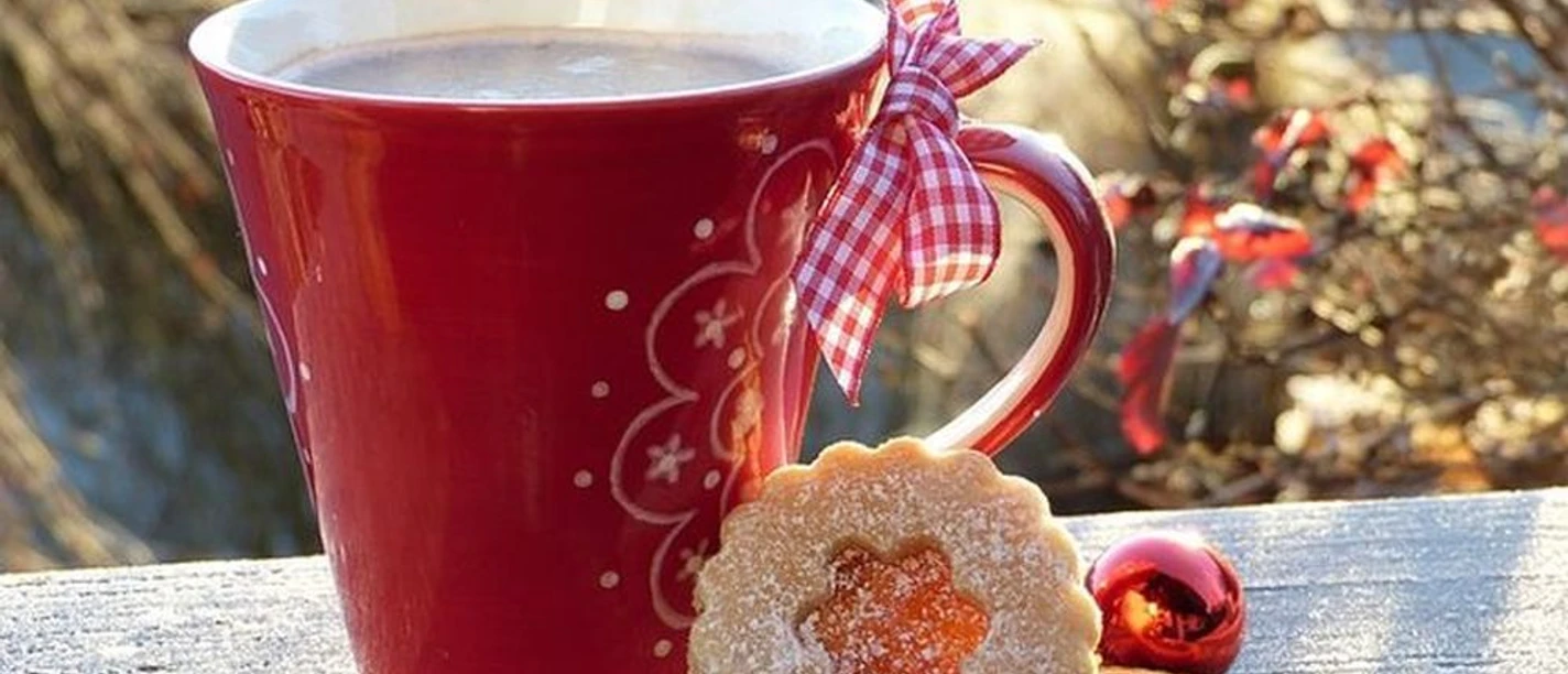Weihnachtsmarkt Rote Weihnachtstasse mit Schleife, Gebäck, Orangenscheibe und Kugel im winterlichen Sonnenlicht.