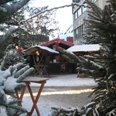 weihnachtsmarkt_winter_hubertusgrimm Verschneiter Weihnachtsmarkt mit Holzbuden, umgeben von Tannenbäumen, stimmungsvoll dekoriert.