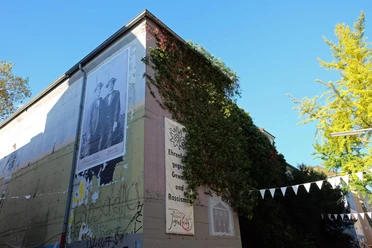BunkerK101 Graffiti-verzierter Bunker mit großen Wandbildern und satt begrünten Ecken unter blauem Himmel.