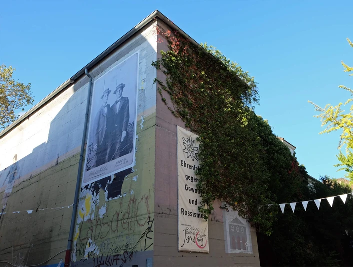 BunkerK101 Graffiti-verzierter Bunker mit großen Wandbildern und satt begrünten Ecken unter blauem Himmel.Graffiti-decorated bunker with large murals and lush green corners under a blue sky.