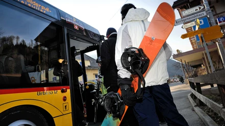 Personen mit Wintersportgeräten steigen in ein Postauto Bus ein