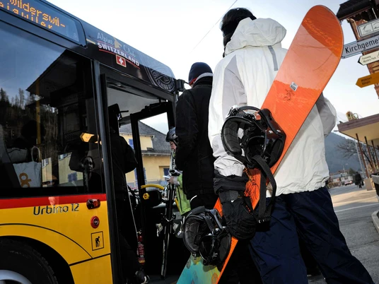 Personen mit Wintersportgeräten steigen in ein Postauto Bus ein
