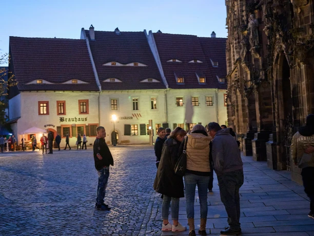 Priesterhäuser_c Foto-Atelier Lorenz.jpg Abenddämmerung auf einem historischen Platz mit Menschen vor älteren Fachwerkbauten.
