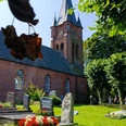 Ev. luth. Kirche Woquard Backsteinkirche Woquard mit spitzem Turm, umgeben von Bäumen und altem Friedhof mit Grabsteinen.
