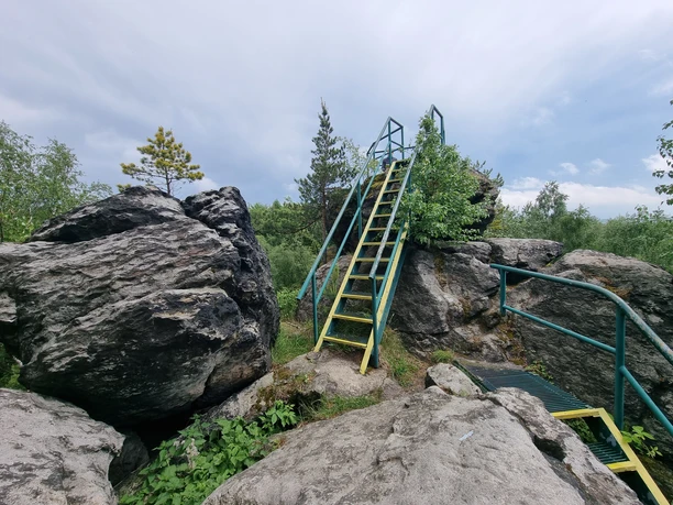 Zeisigstein Gelbe Metallleiter zwischen großen Felsen unter bewölktem Himmel.