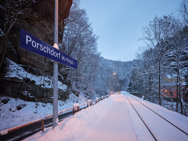 Besneeuwd perron in Porschdorf bij schemering, bord "Porschdorf" zichtbaar.