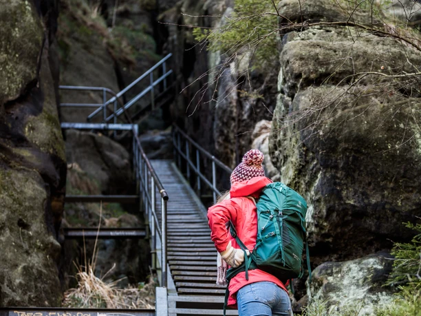 Persoon in rode jas beklimt steile trap in rotsachtige kloof.