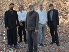 Fünf Personen stehen auf steinigem Untergrund vor einem Hang und blicken ruhig zur Kamera.