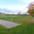 Die Boulebahn liegt umgeben von einer Rasenfläche direkt neben einem Spielplatz. Im Hintergrund ist ein Fußballplatz zu sehen.