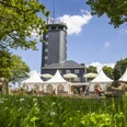 Hohe Bracht Ein markanter grauer Turm, umgeben von weißen Pavillons, vor einer Kulisse aus blühenden Wiesen.A striking gray tower, surrounded by white pavilions, against a backdrop of flowering meadows.Een opvallende grijze toren, omringd door witte paviljoens, tegen een achtergrond van bloeiende weiden.