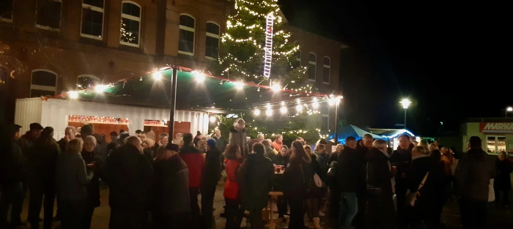 Weihnachten mit dem OBV Apen Menschenmenge bei Nacht auf einem festlich beleuchteten Weihnachtsmarkt vor einem großen Baum.
