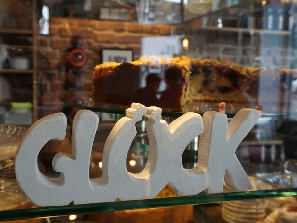 pottschwarz, Mülheim an der Ruhr Dekorativer „GLÜCK”-Schriftzug aus Holz auf einer Café-Theke vor einer Obsttorte