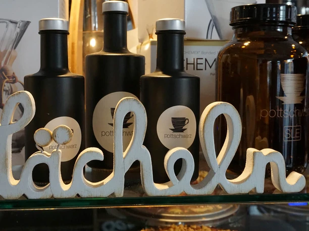 pottschwarz, Mülheim an der Ruhr Auf einer Theke in einem Café stehen Dekoflaschen und ein Holzschriftzug mit dem Wort „Lächeln”.