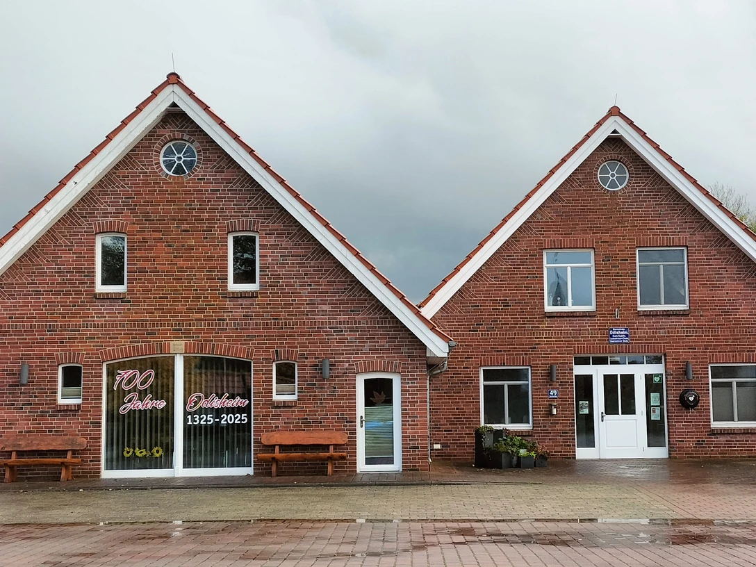 Dorfgemeinschaftshaus Odisheim Zweigeteiltes Backsteingebäude mit rotem Dach und weißen Fensterrahmen unter grauem Himmel.