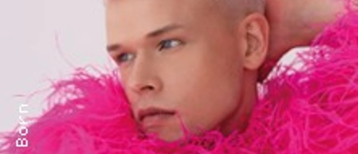Eine Person mit hellblonden Locken trägt ein pinkfarbenes, federndes Outfit und blickt seitwärts.