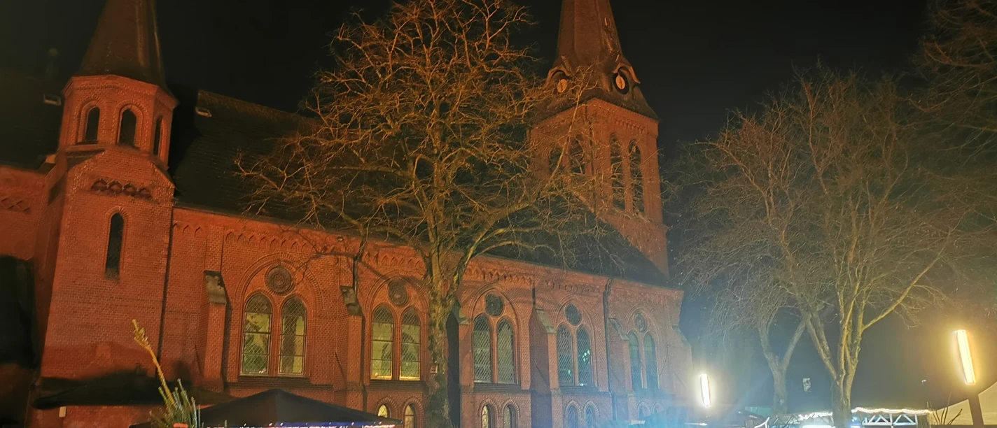 Ummelner Kirche im Dunkeln, davor Weihnachtsmarktstände und Menschen
