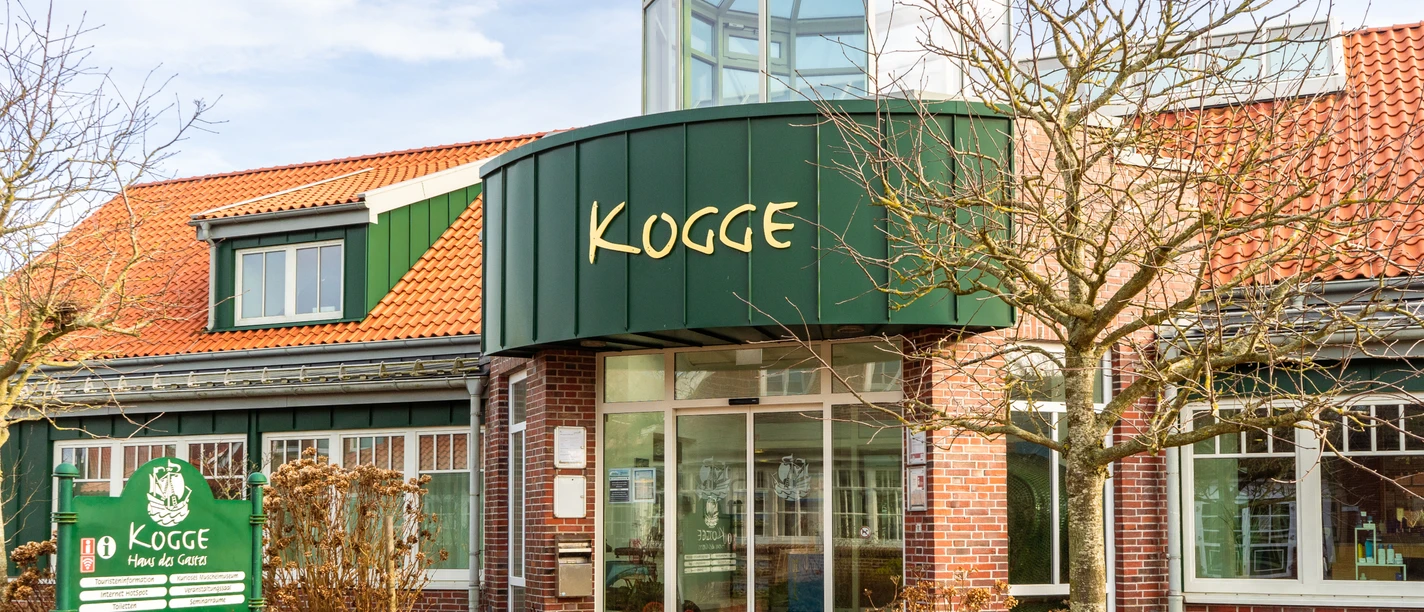 Backsteingebäude mit rotem Dach und grünem Eingangsbereich der Tourist-Information Kogge auf Spiekeroog.