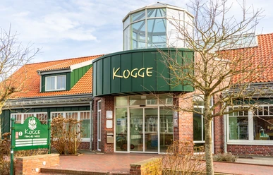 Backsteingebäude mit rotem Dach und grünem Eingangsbereich der Tourist-Information Kogge auf Spiekeroog.