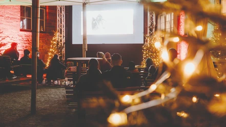 Filmhof - Rathausinnenhof Besucher sehen einen Film im festlich beleuchteten Rathausinnenhof.