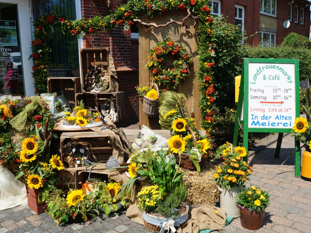 LandfrauenMarkt Ihlienworth Bunte Blumenarrangements mit Sonnenblumen vor dem Eingang des Landfrauenmarkts und Cafés.