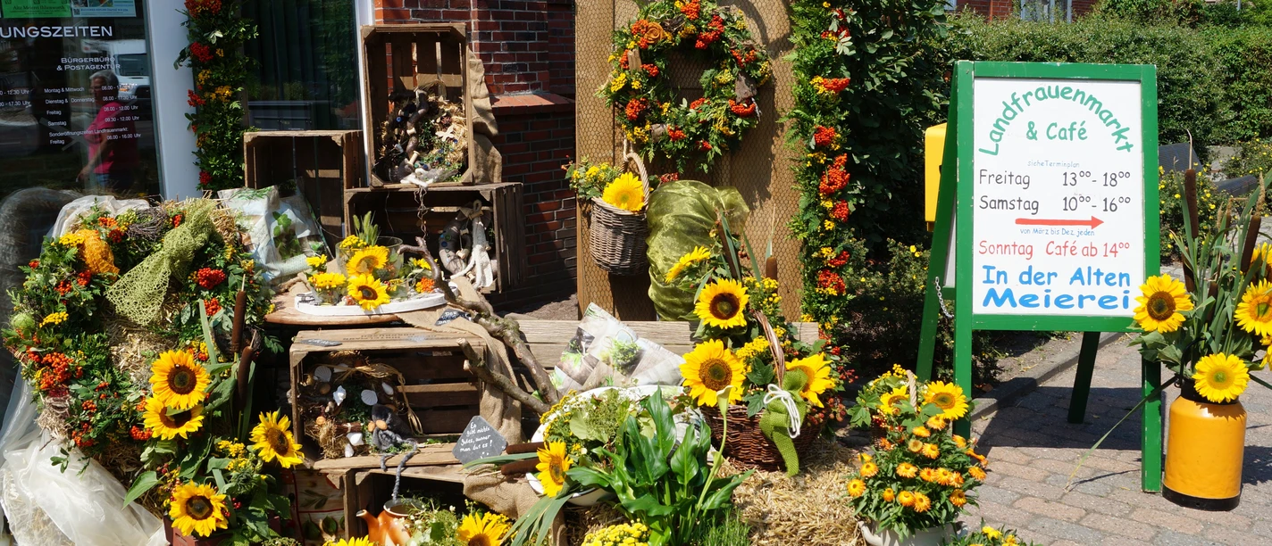 LandfrauenMarkt Ihlienworth Bunte Blumenarrangements mit Sonnenblumen vor dem Eingang des Landfrauenmarkts und Cafés.