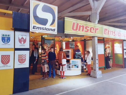 Messestand der Emsland GmbH 1974 in Cloppenburg - Quelle - Kreisarchiv Emsland Ausstellung Emslandplan.jpg Messestand der Emsland GmbH 1974 mit Besuchern und bunten Ausstellungstafeln unter einer Halle