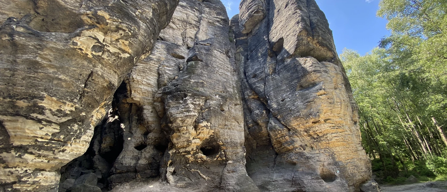 Tyssaer Wände Scogliere di arenaria con grotte e alberi sotto un cielo azzurro.